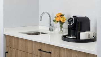 A kitchen with a white countertop, a stainless steel sink, a coffee machine, and a vase with flowers.