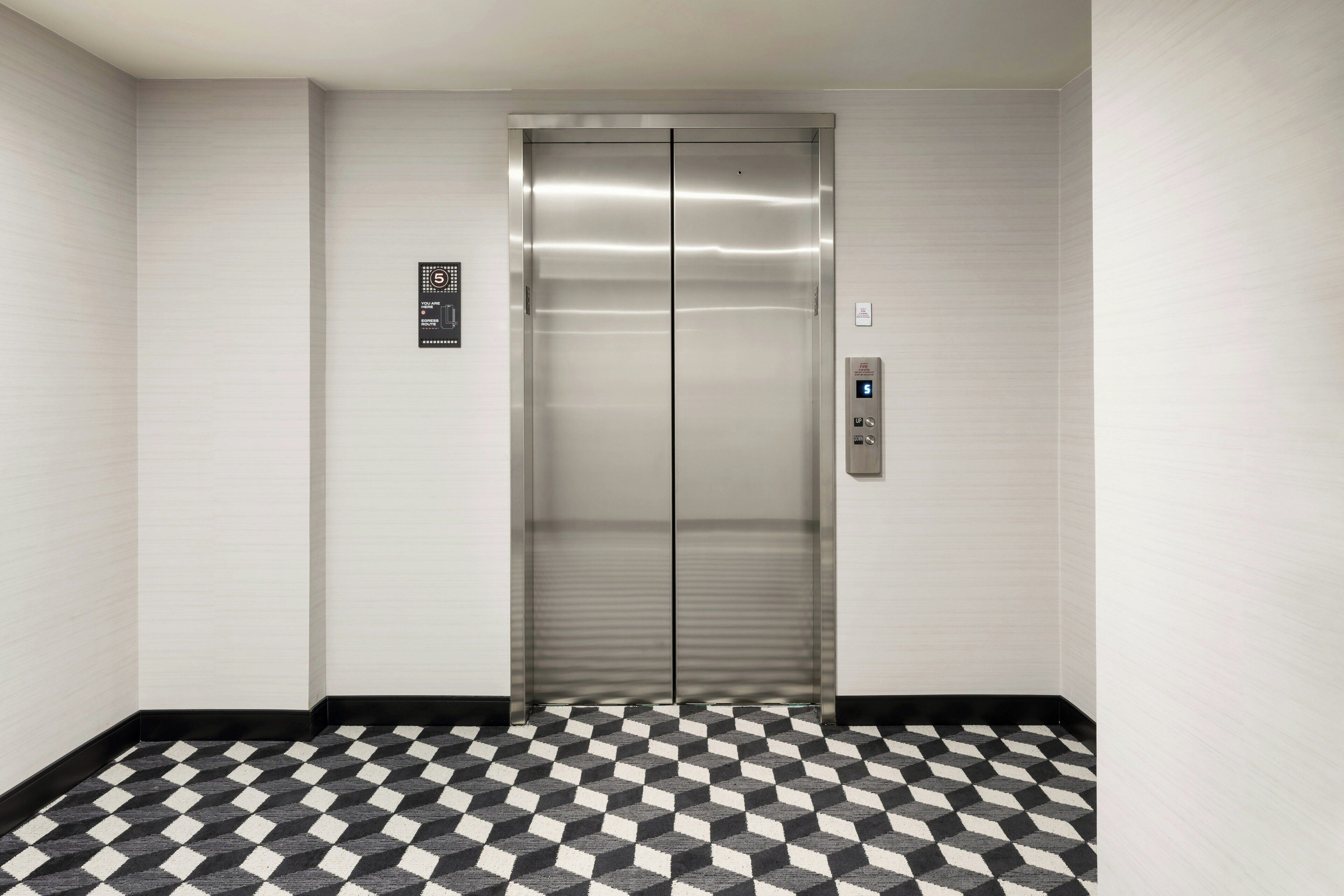 An elevator with a metallic finish, a digital control panel, and a patterned floor.