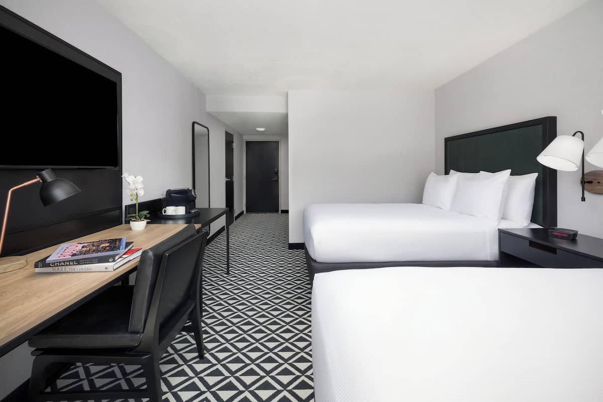 A hotel room with a bed, bedside table, lamp, and a desk with a chair.