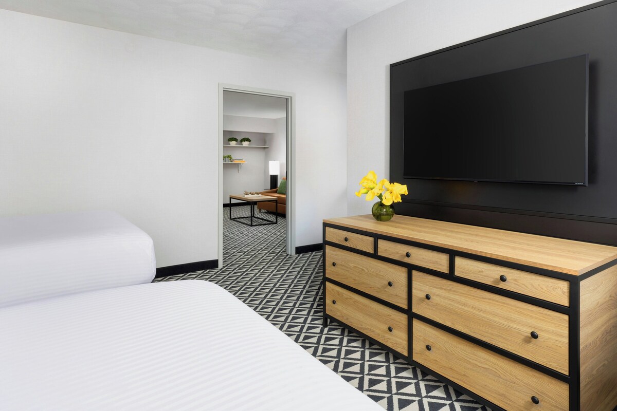 A hotel room with a bed, a dresser with drawers, a flat-screen TV mounted on the wall, and a patterned floor.