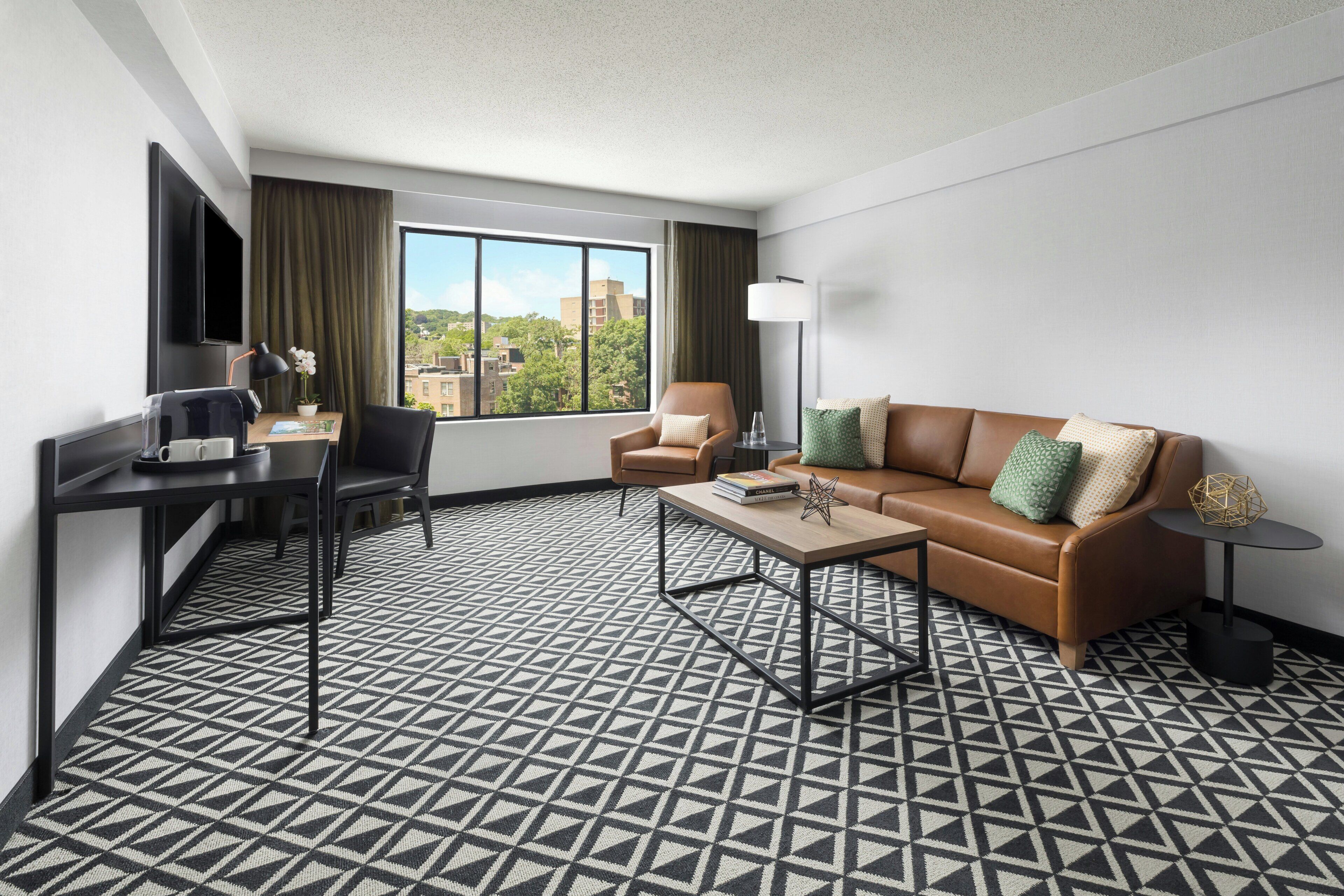 Una habitación de hotel con sofá, escritorio, silla, mesa de centro y televisor.