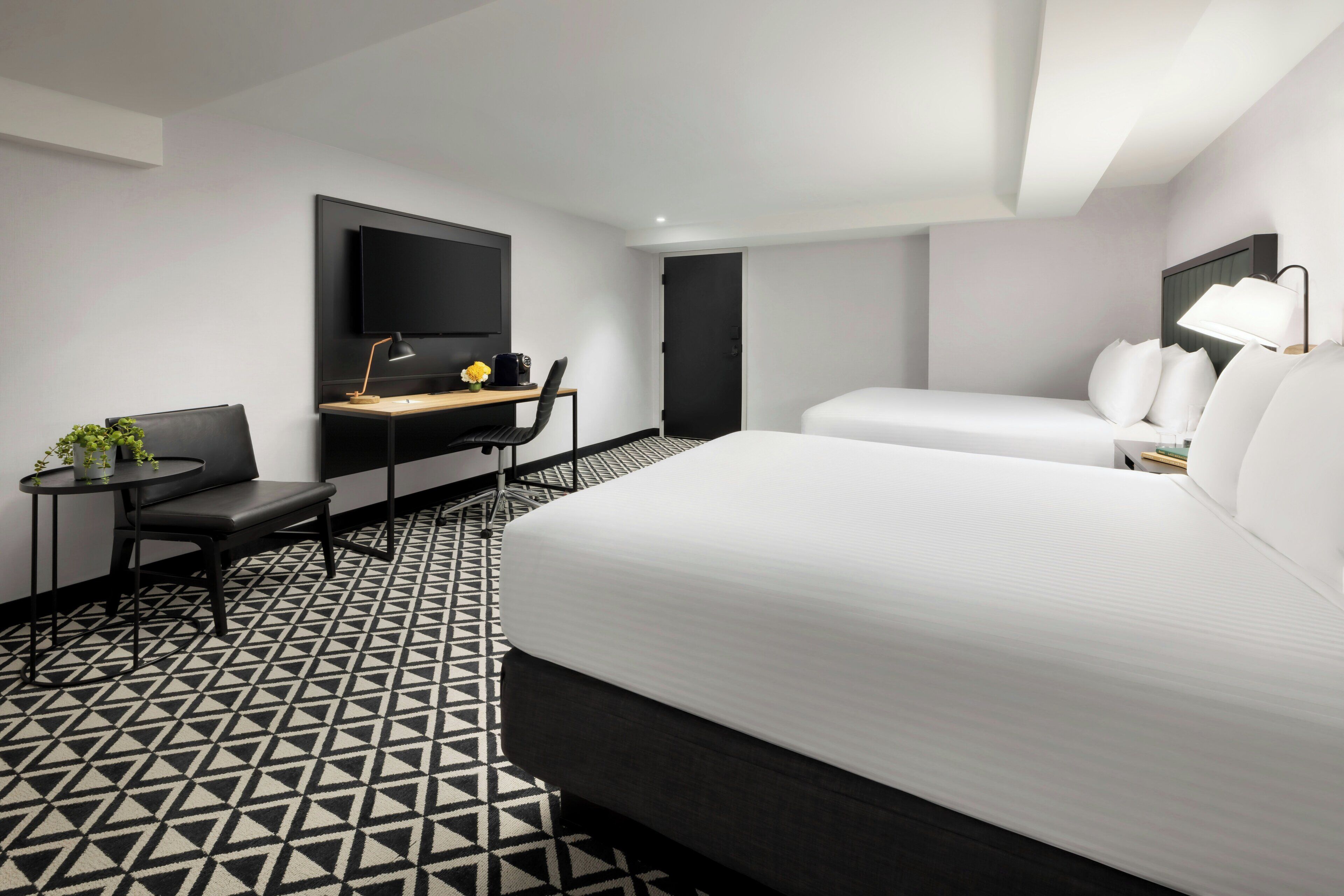 Une chambre d’hôtel avec un lit, un bureau, une chaise, une télévision et un sol à motifs.