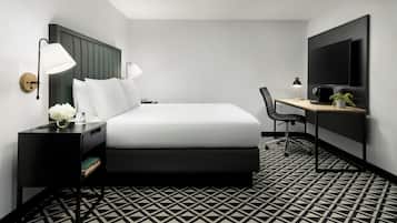 A hotel room with a bed, bedside tables, a desk, a chair, a TV, and a patterned floor.