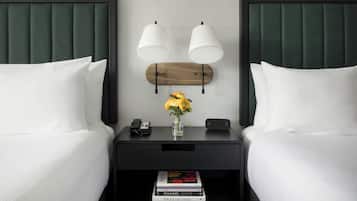 Une chambre d’hôtel avec deux lits, une table de chevet avec une lampe, un téléphone, un vase avec des fleurs et un livre sur la table de chevet.