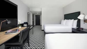 Habitación de hotel con escritorio, dos camas, televisor y piso con diseño.