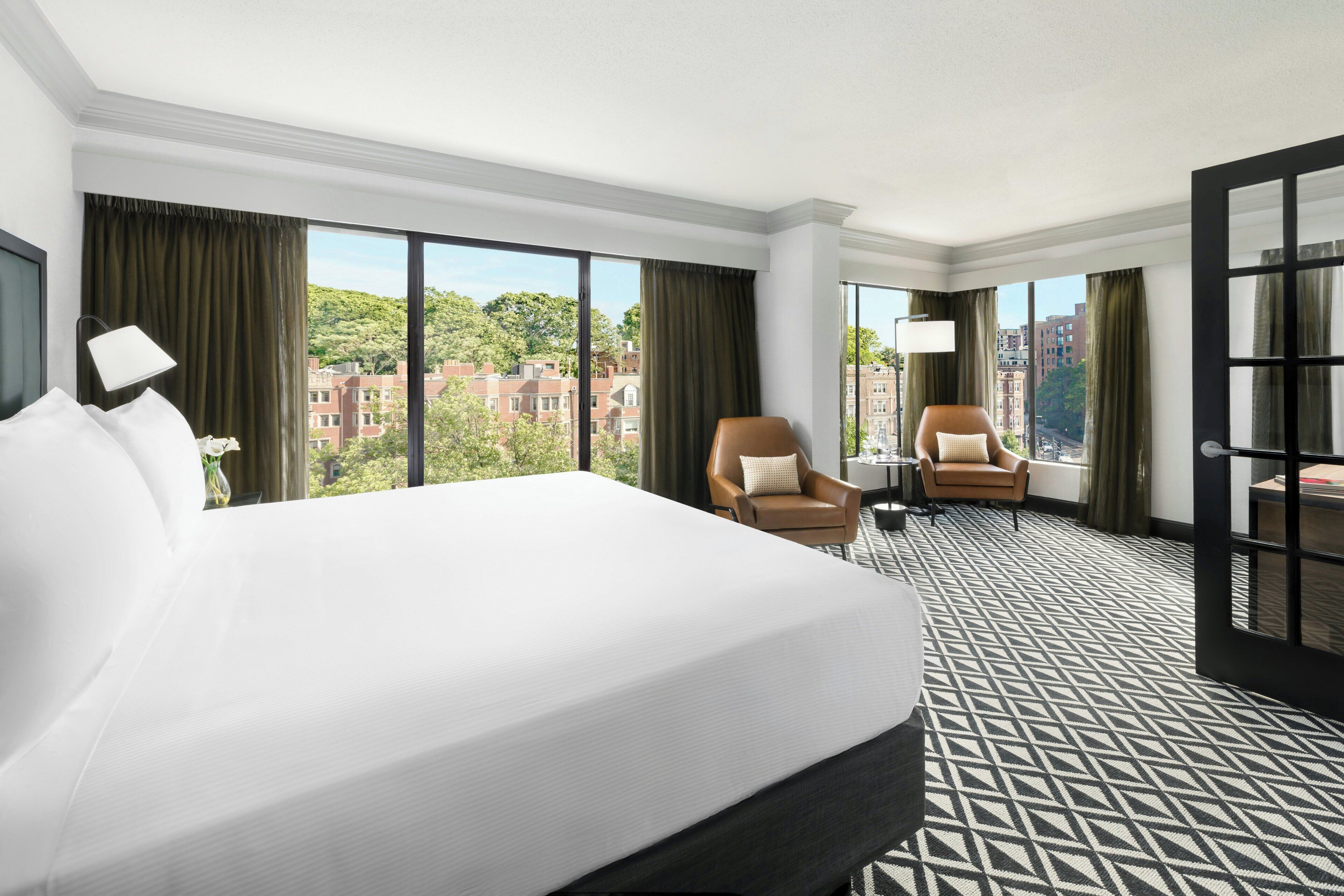 Une chambre d’hôtel avec un grand lit, deux fauteuils, une petite table et une vue sur le paysage urbain.