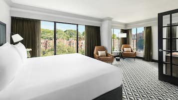Une chambre d’hôtel avec un grand lit, deux fauteuils, une petite table et une vue sur le paysage urbain.
