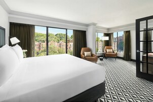 Habitación de hotel con una cama grande, dos sillones, una mesita y vista a la ciudad.