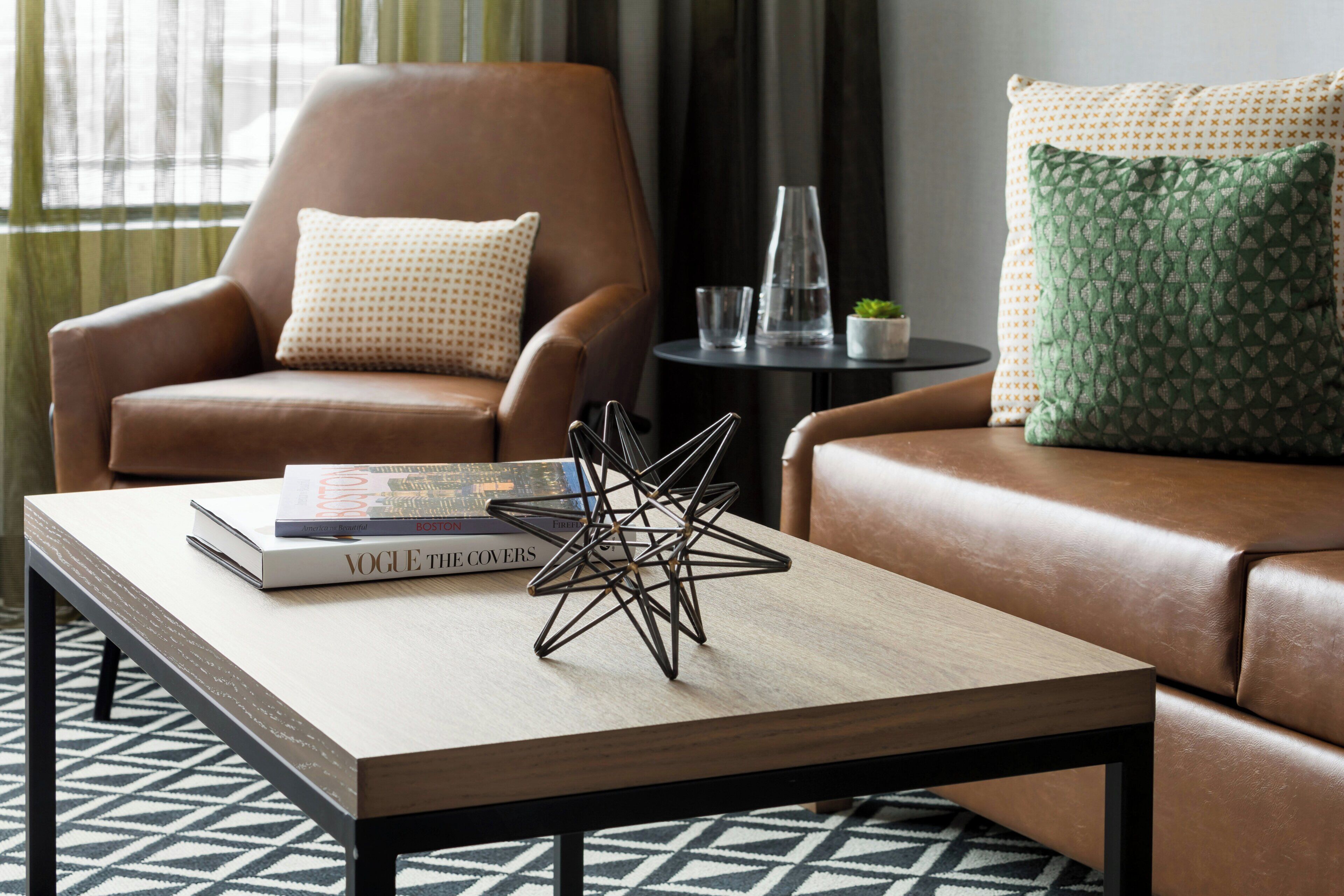 A modern living room with a leather armchair, a sofa, a coffee table with books and a decorative metal sculpture, and a patterned rug.