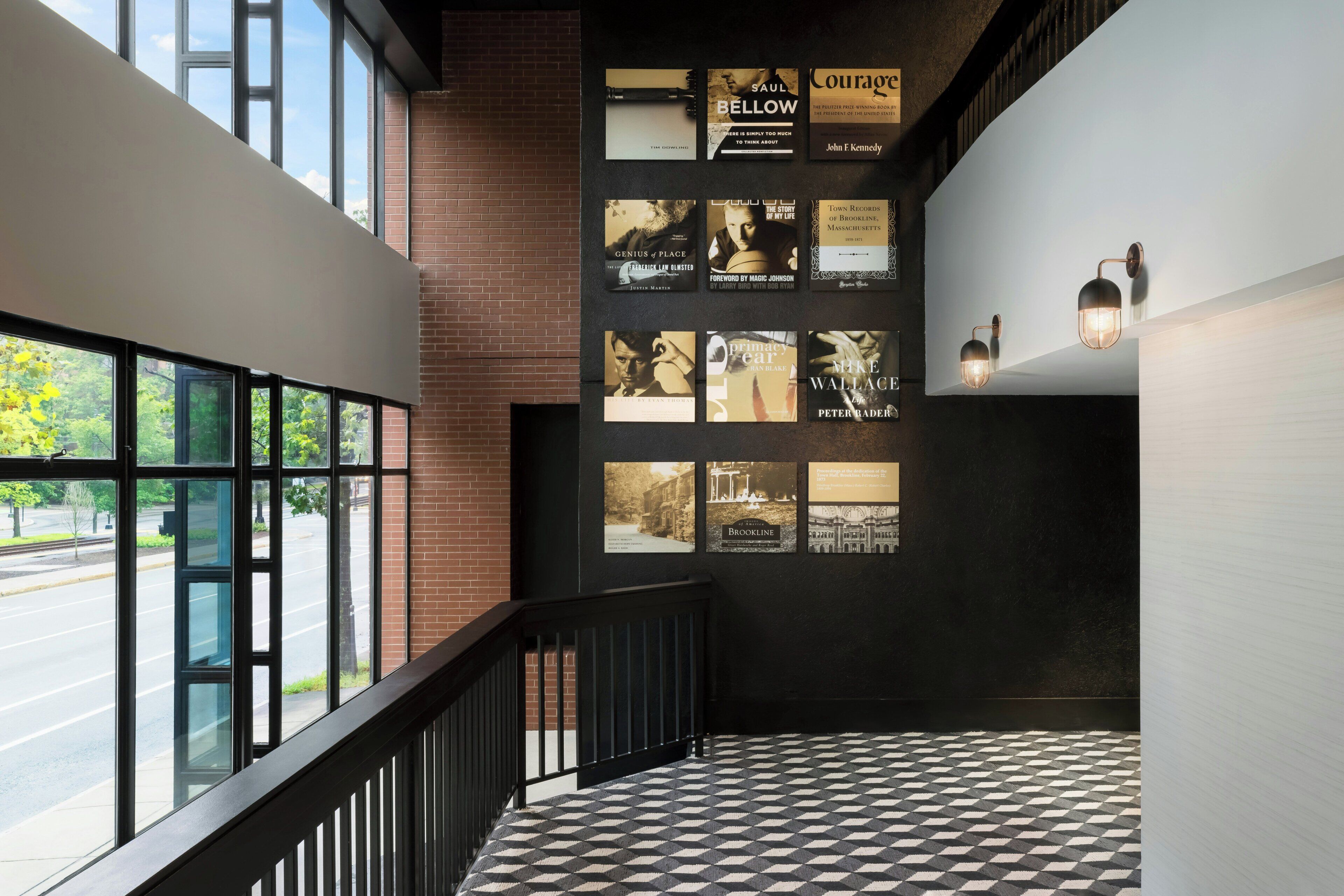 A staircase with a black and white checkered floor, a brick wall, and a series of framed items on the wall.
