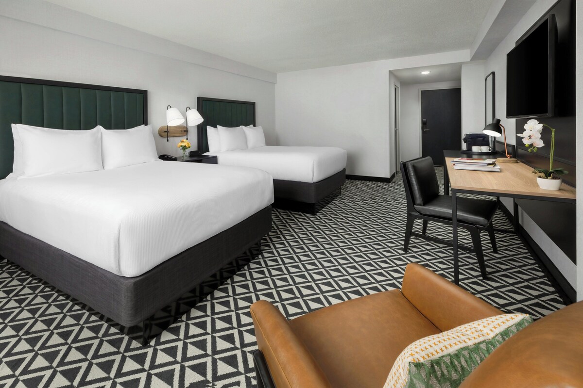 Une chambre d’hôtel avec un grand lit, deux tables de chevet, un bureau avec une chaise et un téléviseur fixé au mur.