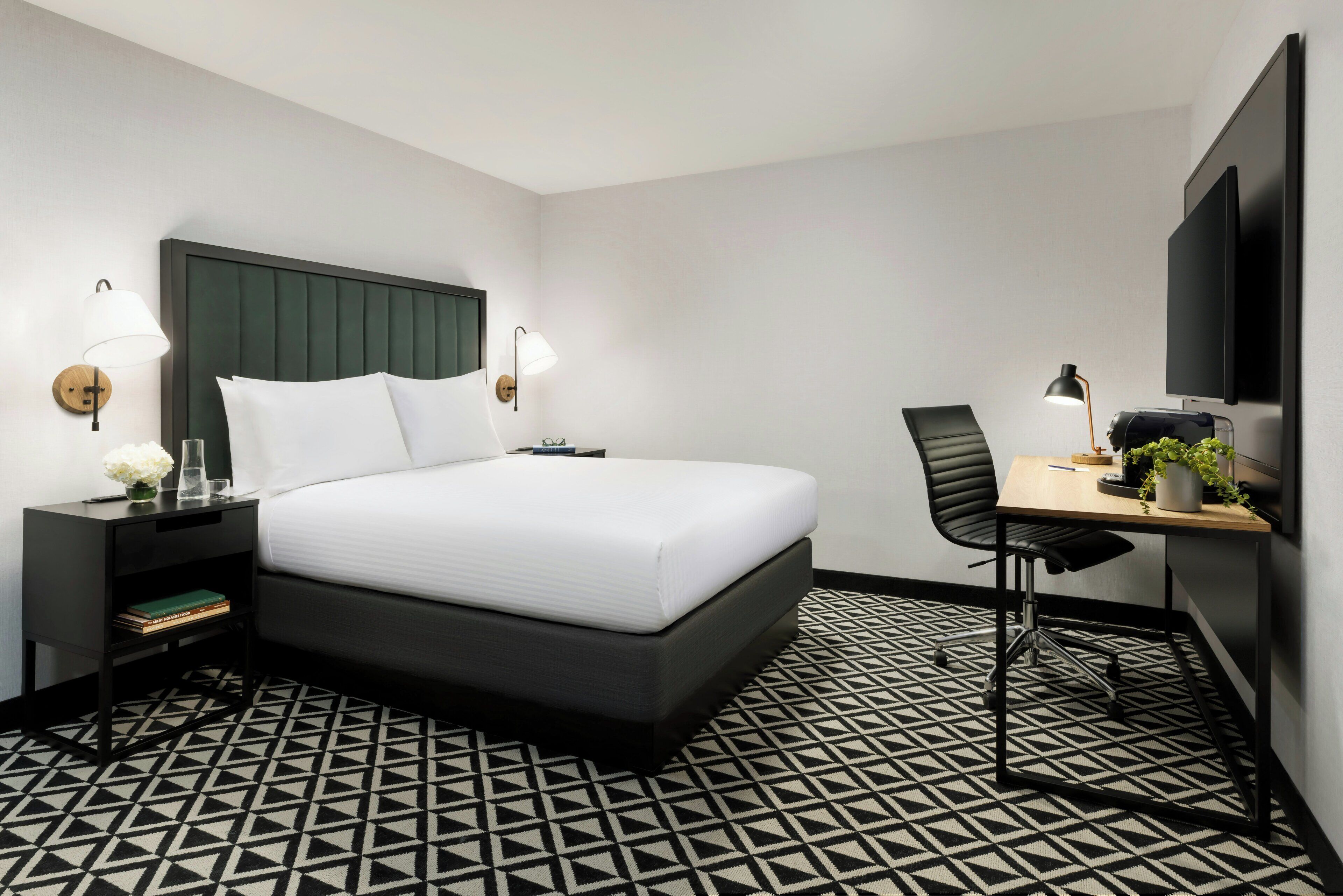 Habitación de hotel con cama, mesitas de noche, escritorio con silla, televisión de pantalla plana y suelo estampado.