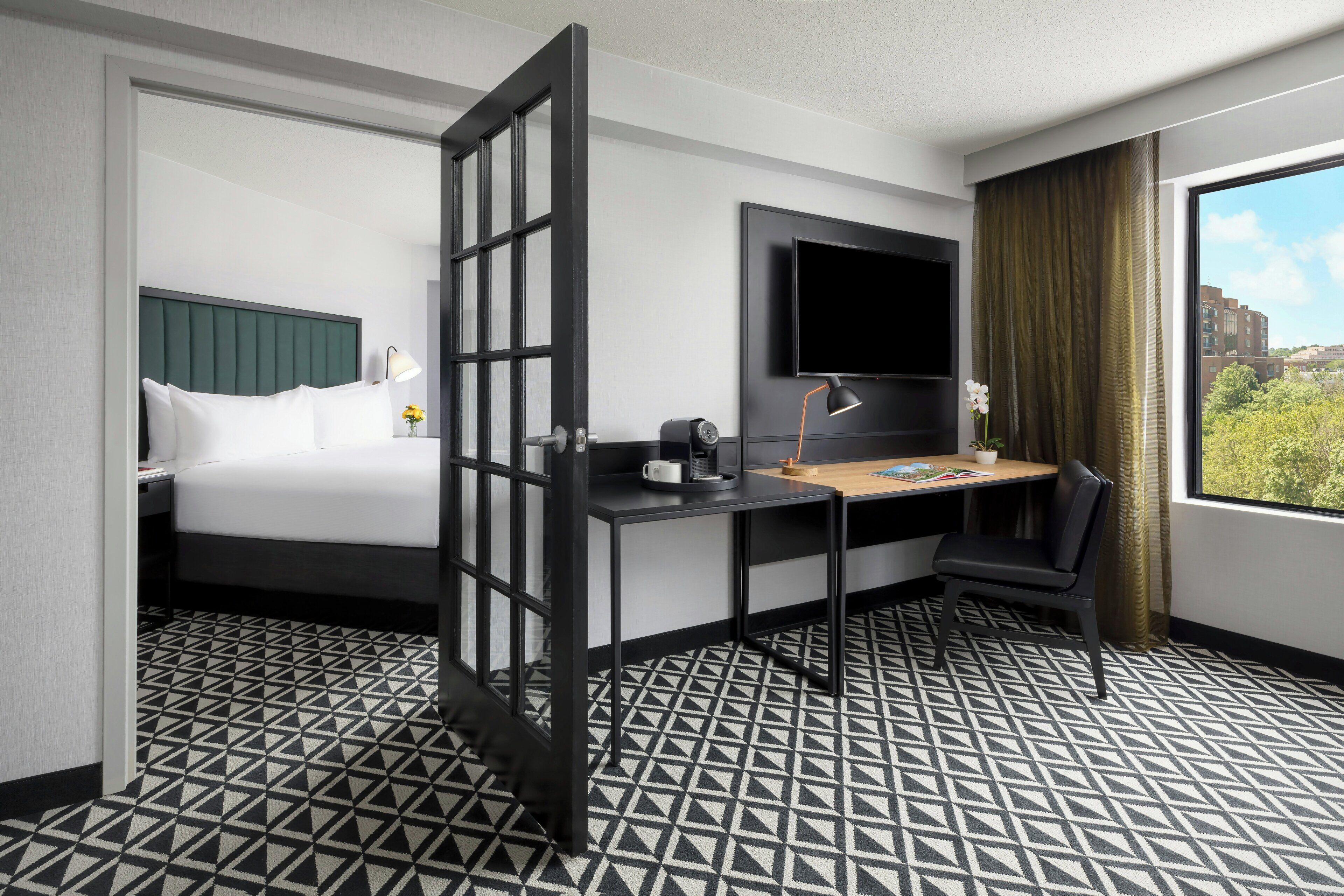 A hotel room with a bed, desk, chair, TV, and a window with a view.