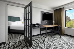 Habitación de hotel con cama, escritorio, silla, televisor y ventana con vistas.
