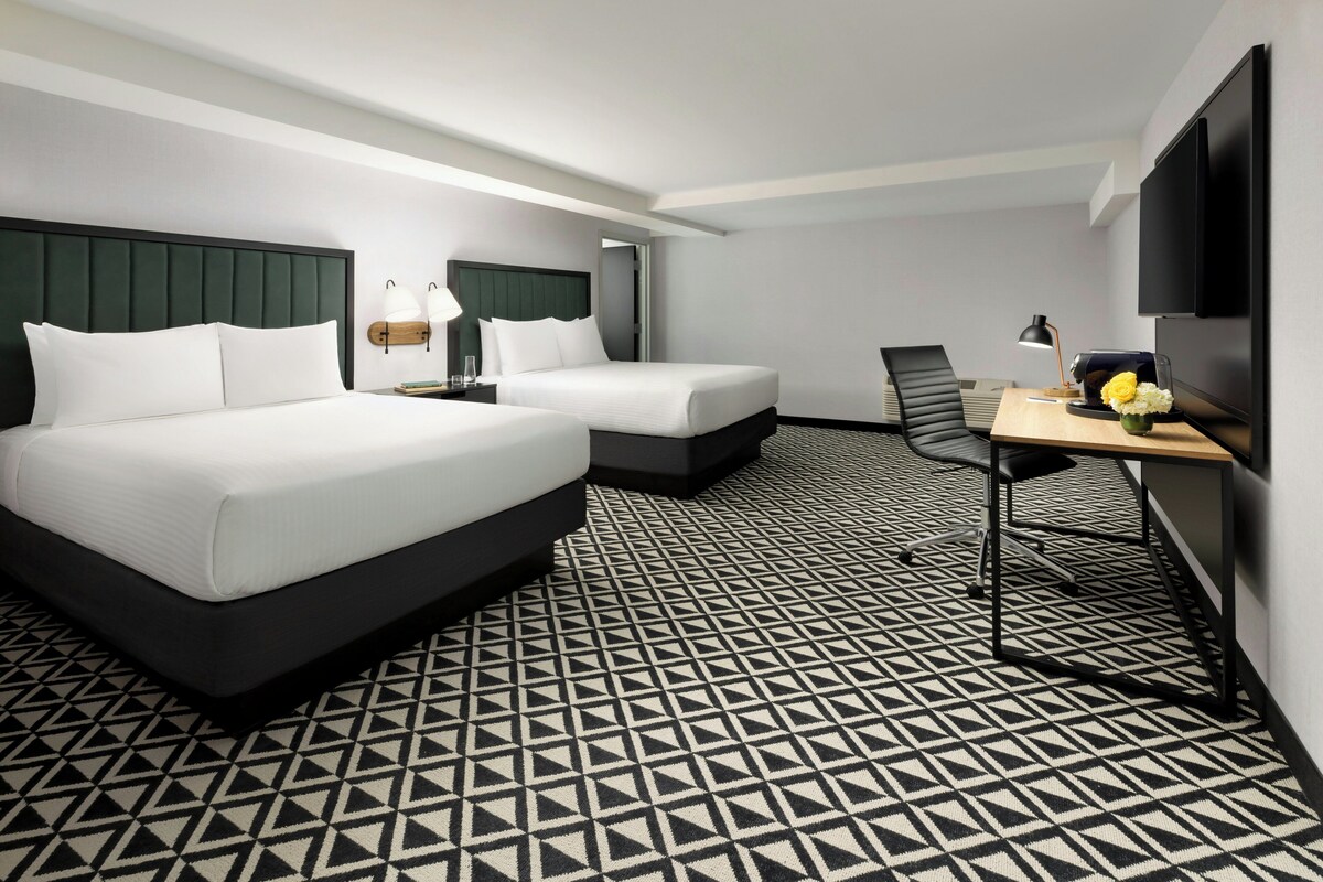 Une chambre d’hôtel avec deux lits, un bureau, une chaise, une télévision et un sol à motifs.
