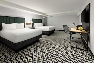Habitación de hotel con dos camas, un escritorio, una silla, un televisor y piso con estampado.