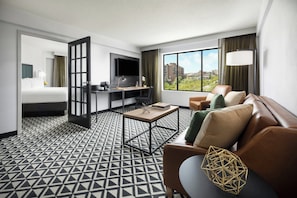 A hotel room with a bed, a desk, a sofa, and a large window offering a city view.
