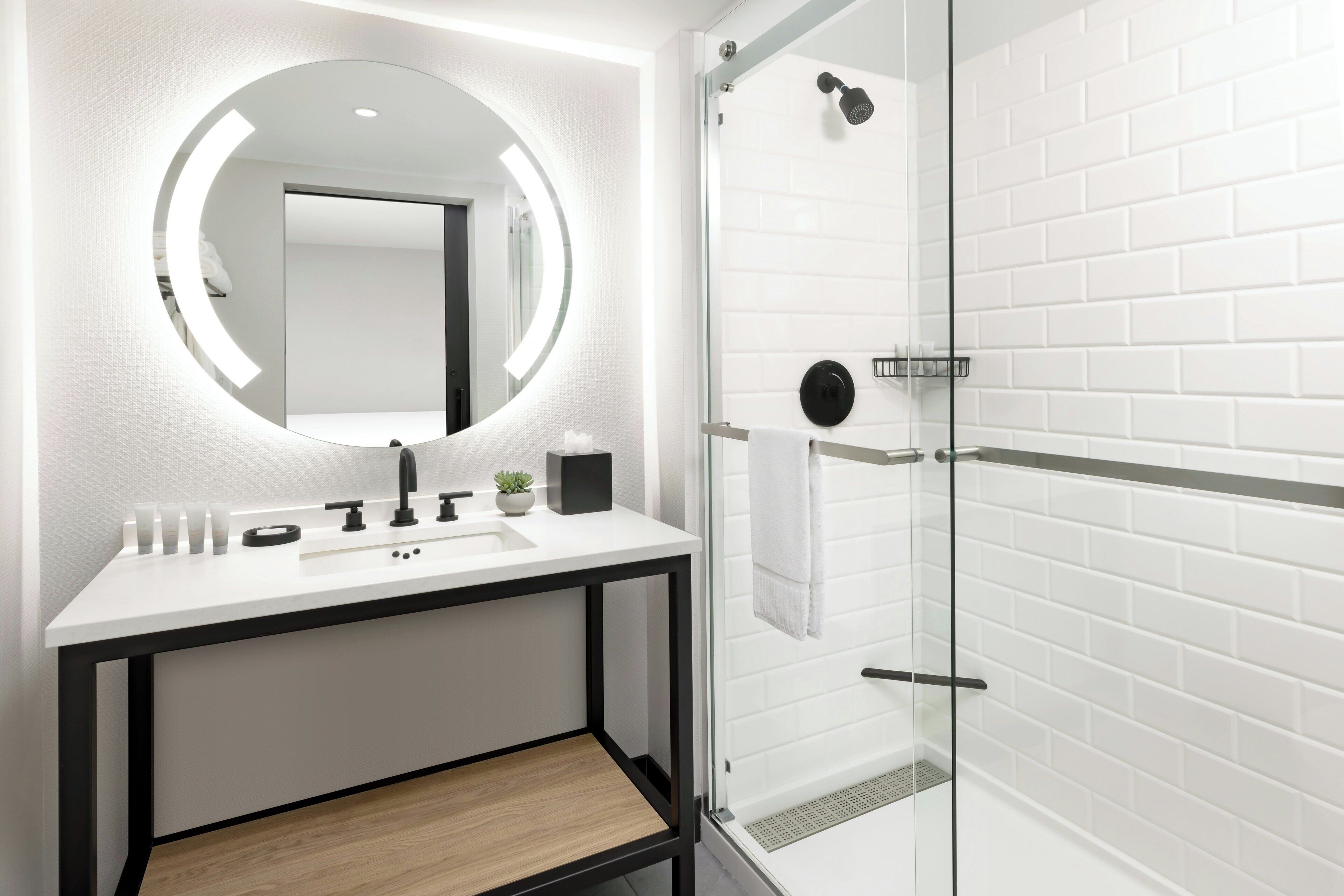 A modern bathroom with a white tiled shower, a round mirror, and a minimalist sink area.