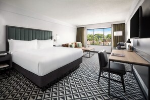 Een hotelkamer met een groot bed, een bureau met stoel, een televisie en een raam met uitzicht op gebouwen.