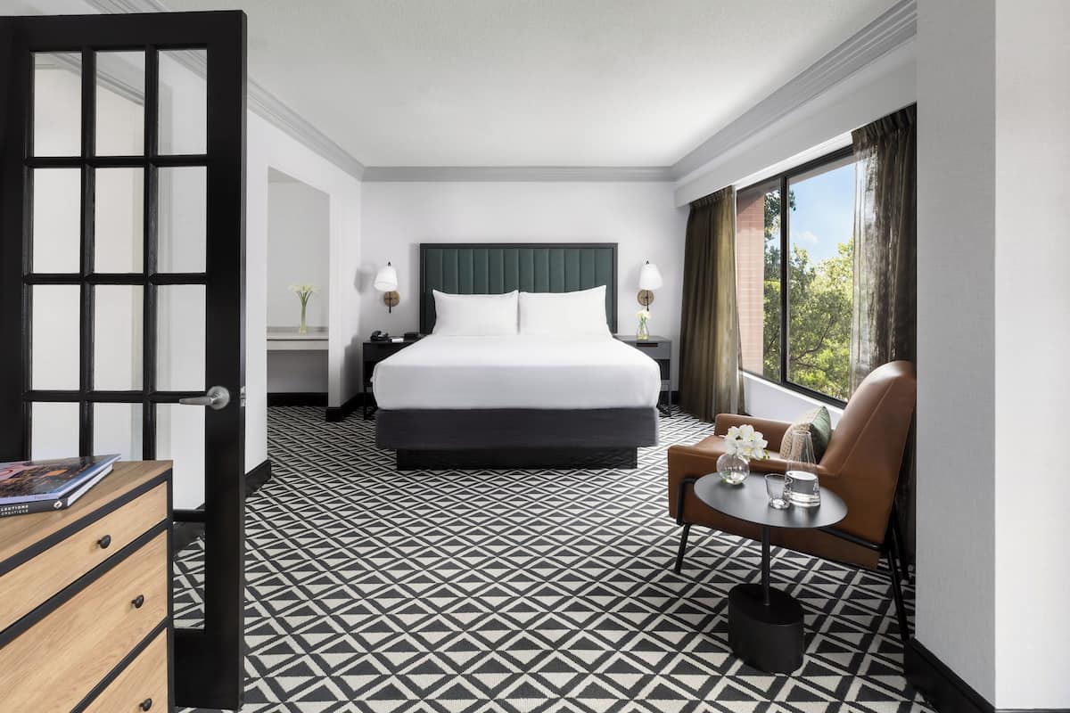 A hotel room with a large bed, a desk, a chair, and a window with curtains.