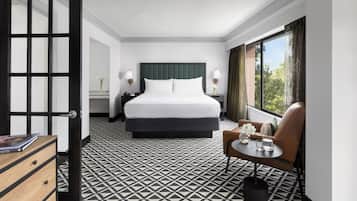 Quarto de hotel com uma cama grande, uma escrivaninha, uma cadeira e uma janela com cortinas.
