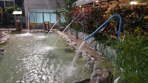 Un área de aguas termales con múltiples chorros, un camino de piedra y abundante vegetación.