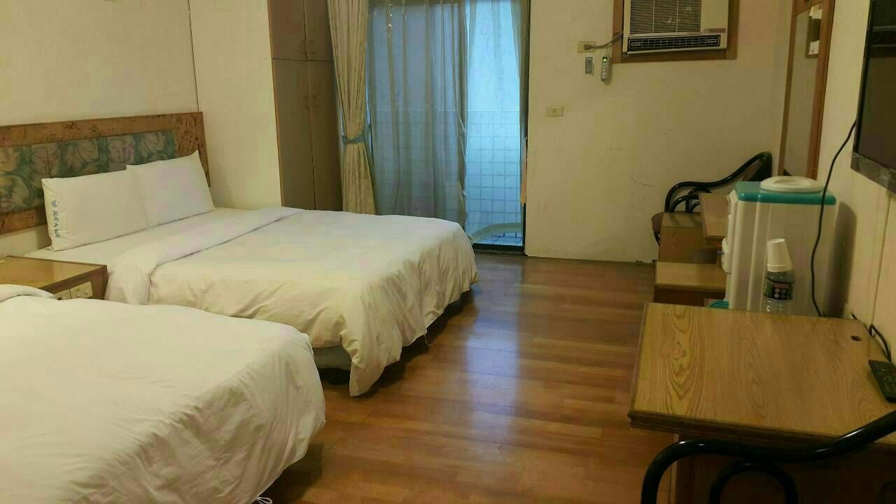 A hotel room with two beds, a wooden desk, a chair, a TV, and a window with curtains.