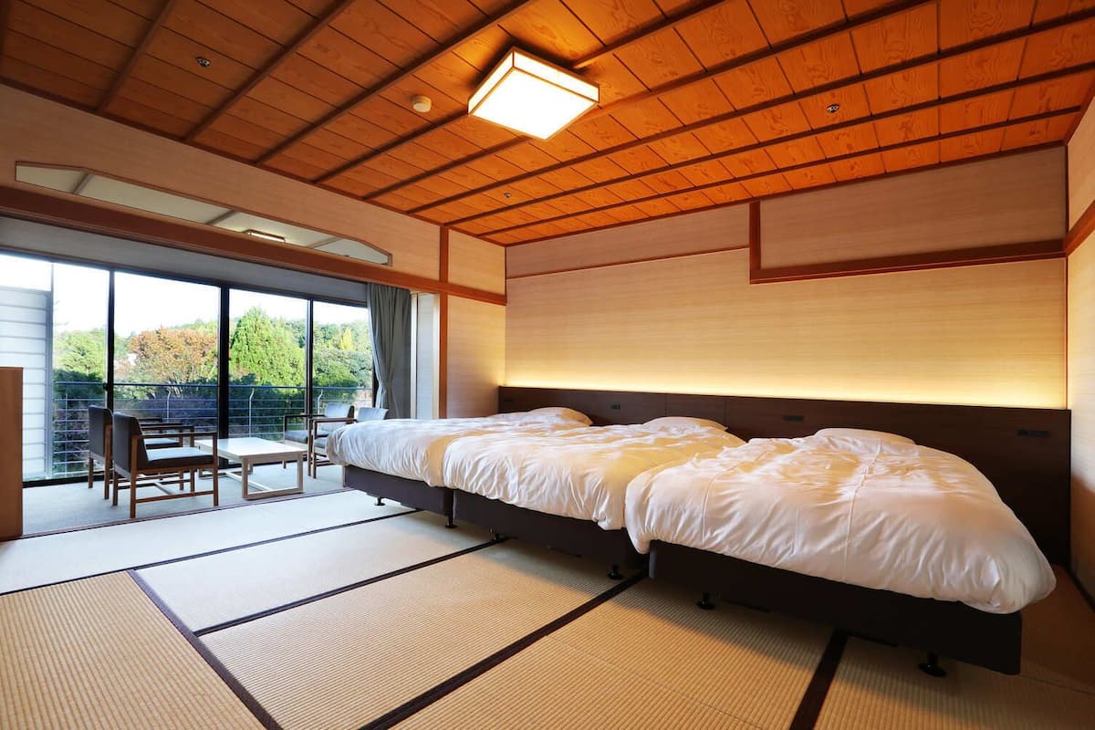 A hotel room with a large bed, a balcony with seating, and a view of the outdoors.