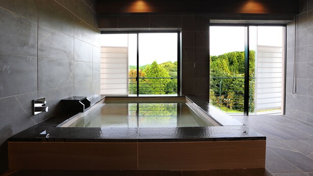 A modern bathroom with a glass-enclosed bathtub, large windows, and a view of greenery outside. - Manten no Tsujinoya (Komatsu)