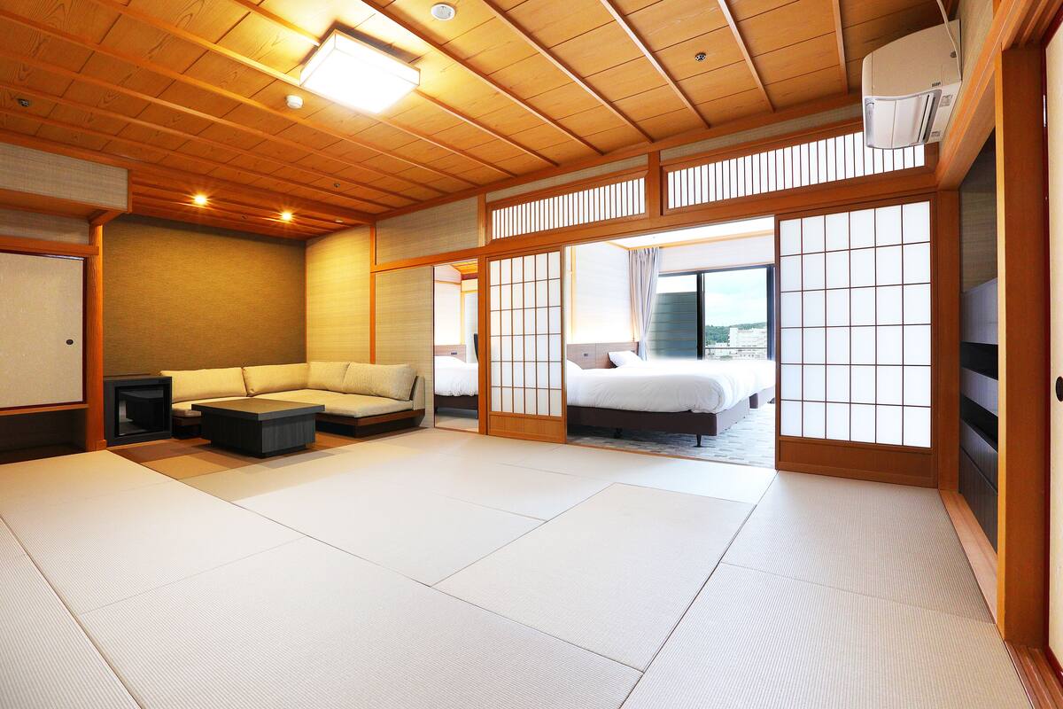 A traditional Japanese-style room with tatami flooring, a low wooden bed, a sofa, and a sliding door leading to a balcony.