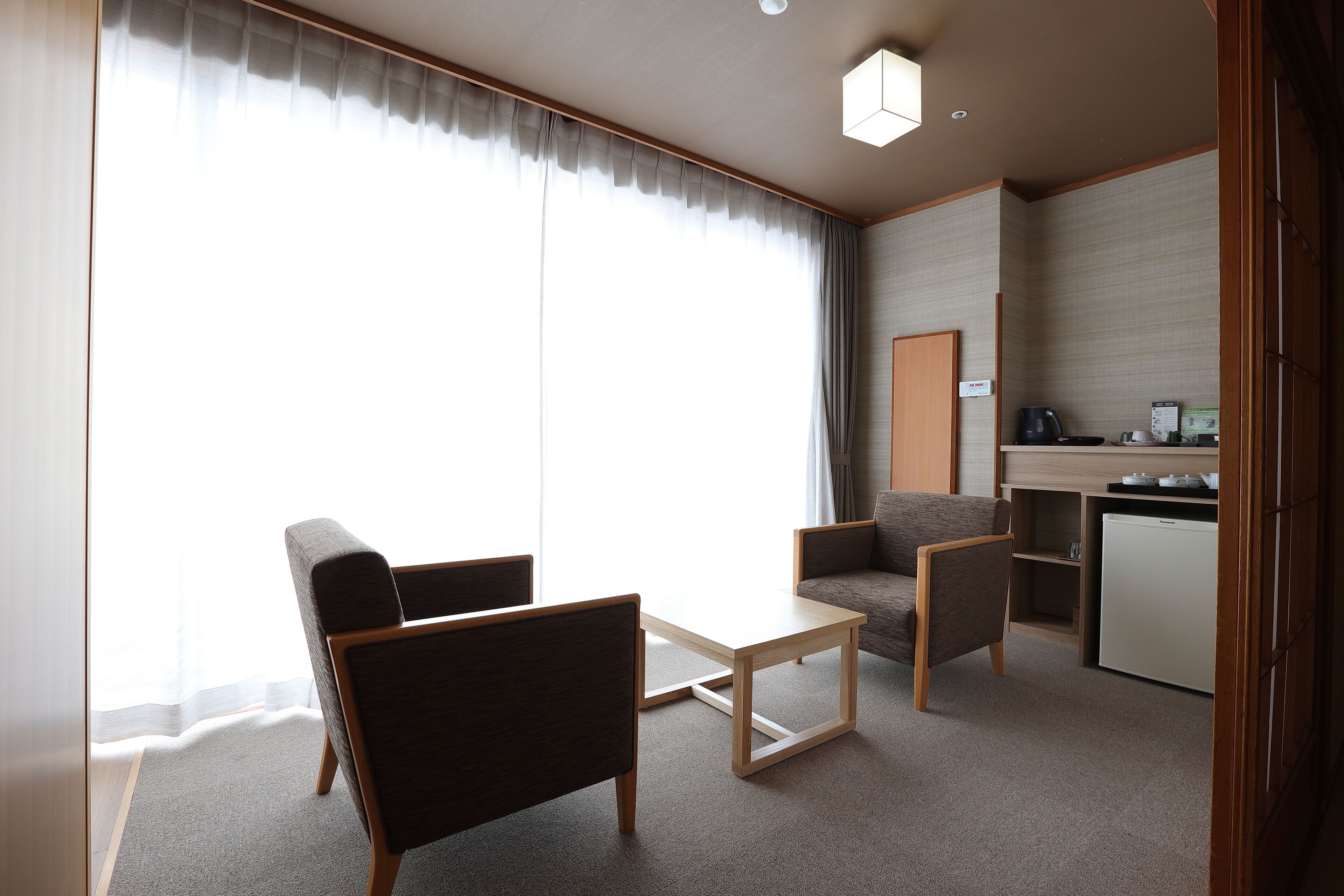 Una habitación de hotel moderna con sofá, sillones, una mesita y una kitchenette.