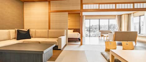 A modern interior with a sofa, a coffee table, and a dining table. There is a view of a snowy landscape through large windows.