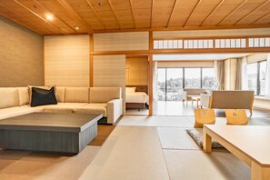A modern interior with a sofa, a coffee table, and a dining table. There is a view of a snowy landscape through large windows. - Manten no Tsujinoya (Komatsu)