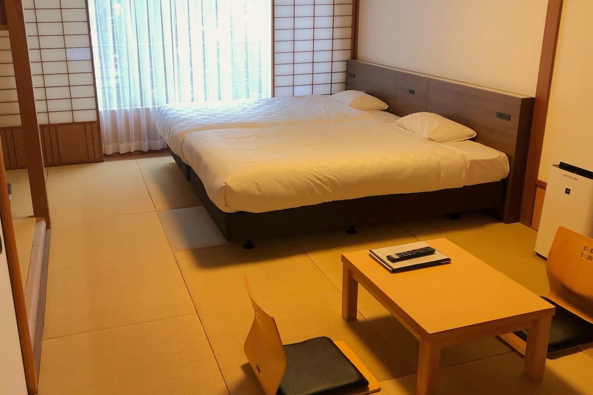 A hotel room with a bed, a desk, a chair, and a window with blinds.