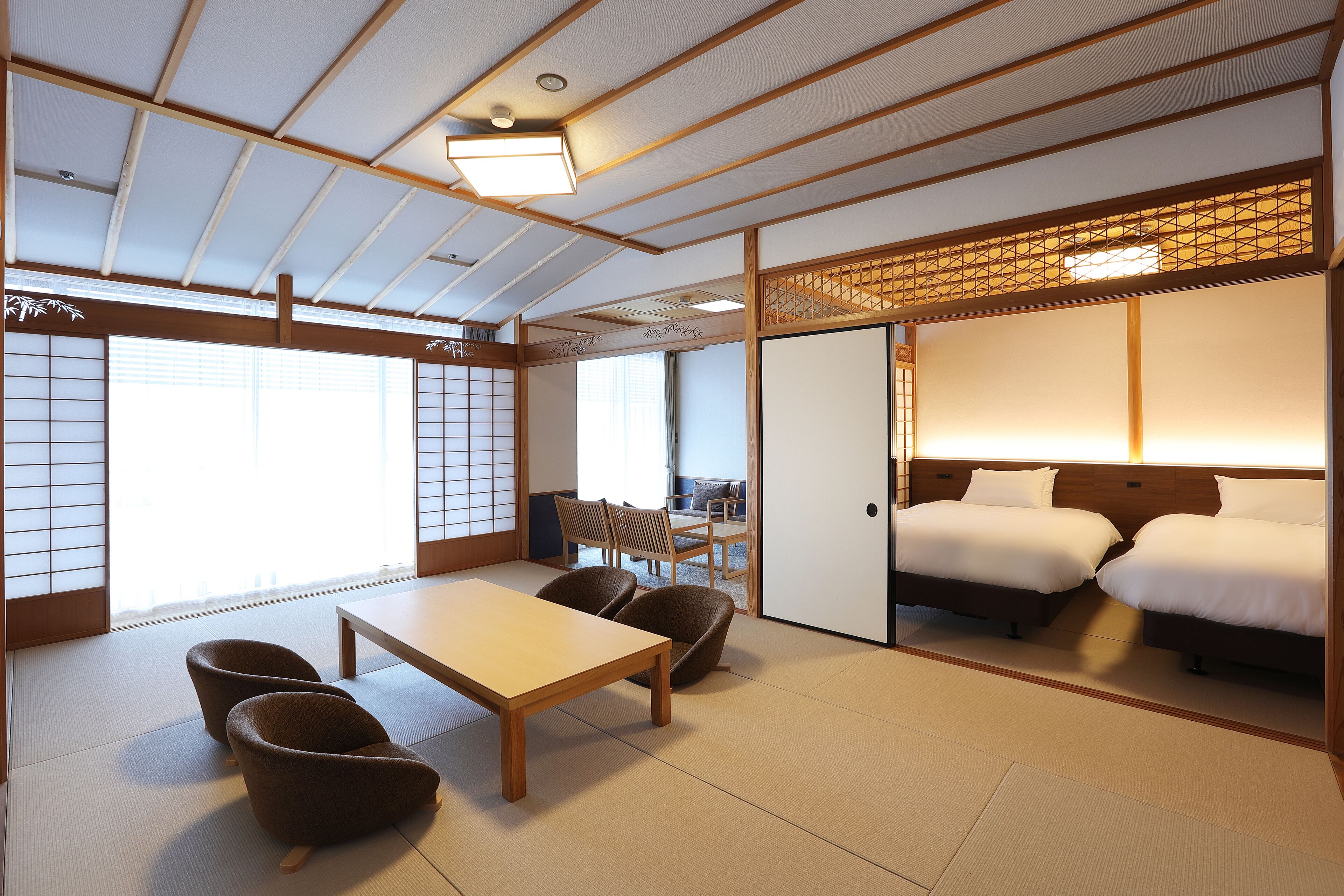 A traditional Japanese room with tatami flooring, a low table, two chairs, a bed, and sliding doors.