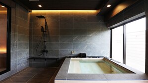 A modern bathroom with a large bathtub, a shower area, and a window providing natural light. - Manten no Tsujinoya (Komatsu)