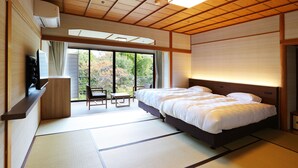 A traditional Japanese-style bedroom with tatami flooring, a large bed, a desk, and a television. - Manten no Tsujinoya (Komatsu)