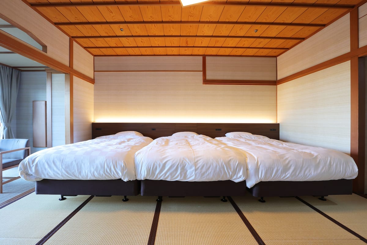 A hotel room with a large bed, wooden ceiling, and tatami flooring.
