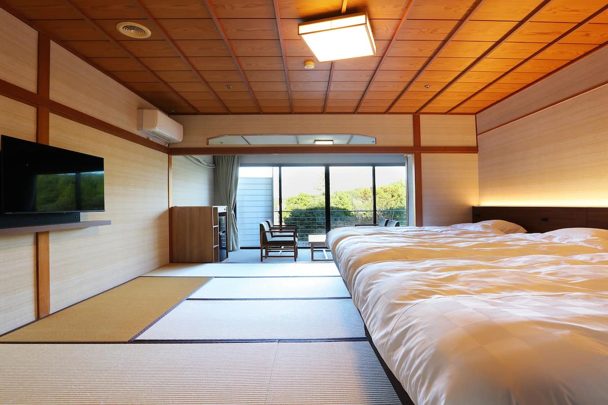 Quarto de hotel com uma cama grande, televisão e porta deslizante para uma varanda.
