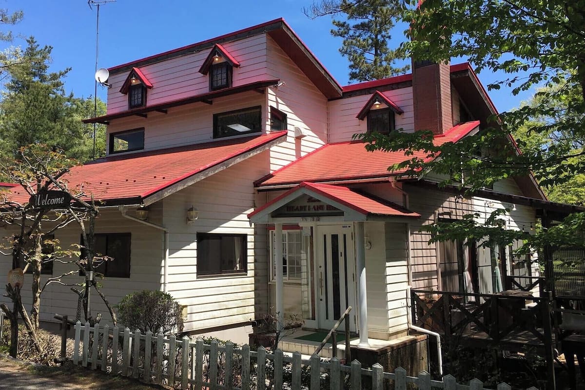 A two-story house with a red roof, a white picket fence, and a 'Welcome' sign.