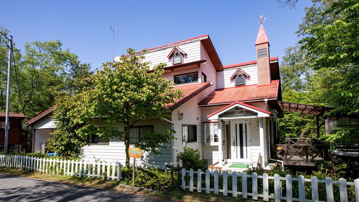 A two-story house with a red roof, a white picket fence, and a small porch.