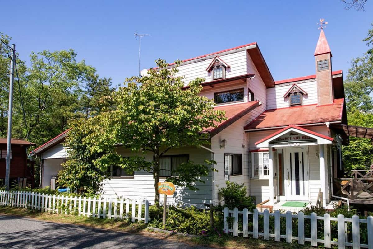 A two-story house with a red roof, a white picket fence, and a small porch.