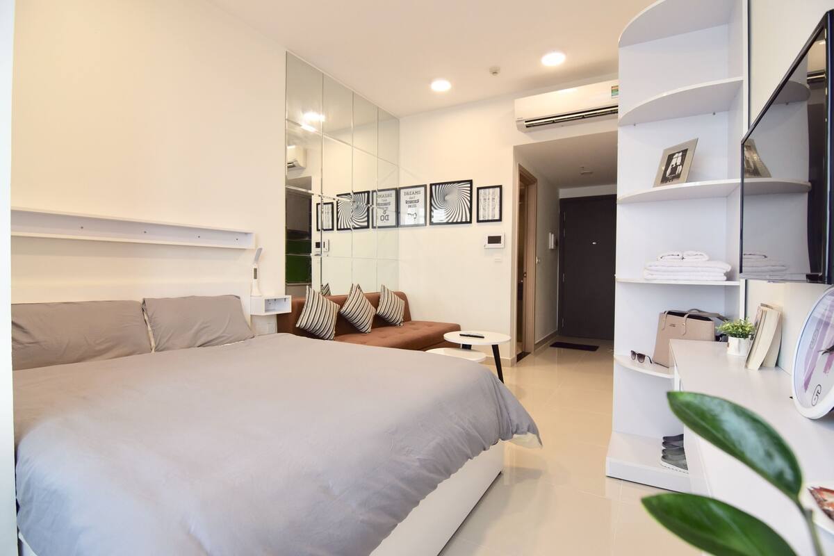 Un dormitorio moderno con una cama grande, un rincón de descanso, un tocador con espejo y una estantería.