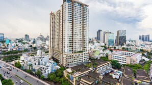 Un edificio de gran altura con varios pisos, rodeado por una zona urbana densa con diferentes edificios y una calle concurrida.