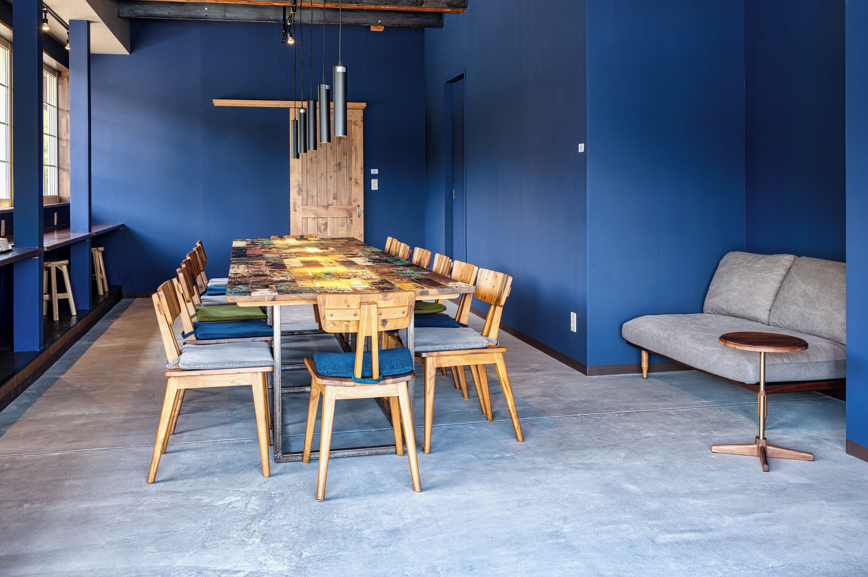 A conference room with a long table and wooden chairs, a grey sofa, and a wooden bench along the wall.
