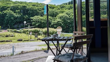 Ein überdachter Außenbereich mit Tisch und Bänken, mit Blick auf eine üppige grüne Landschaft und eine kurvenreiche Straße.