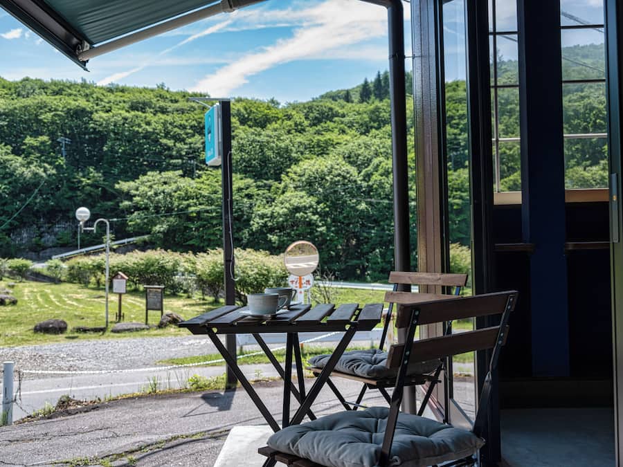 Ein überdachter Außenbereich mit Tisch und Bänken, mit Blick auf eine üppige grüne Landschaft und eine kurvenreiche Straße.