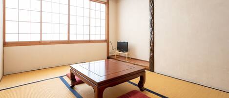 A tatami mat room with a low wooden table and a television on a small stand.