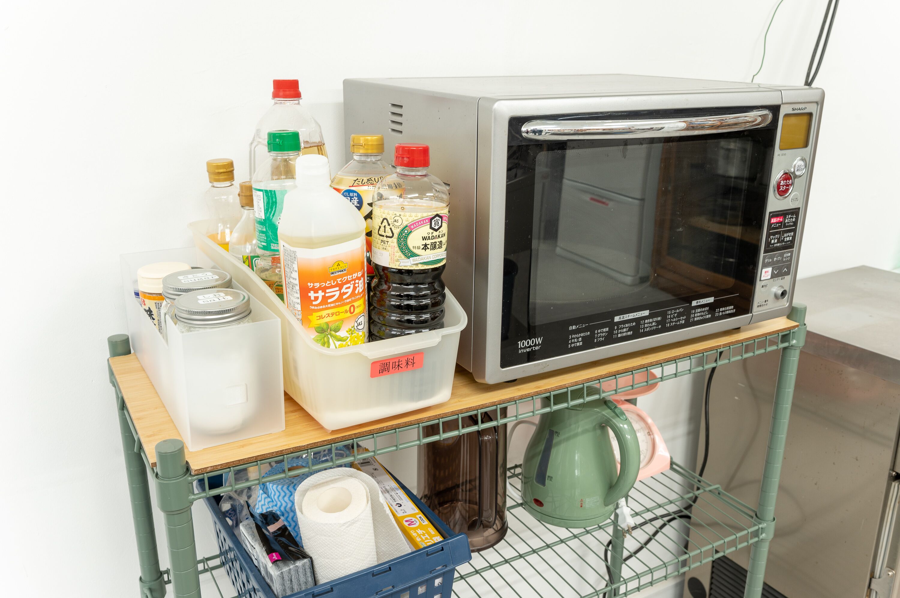 Un microondas sobre una estantería con diversos utensilios de cocina y un recipiente de salsas.