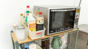 Un microondas sobre una estantería con diversos utensilios de cocina y un recipiente de salsas.